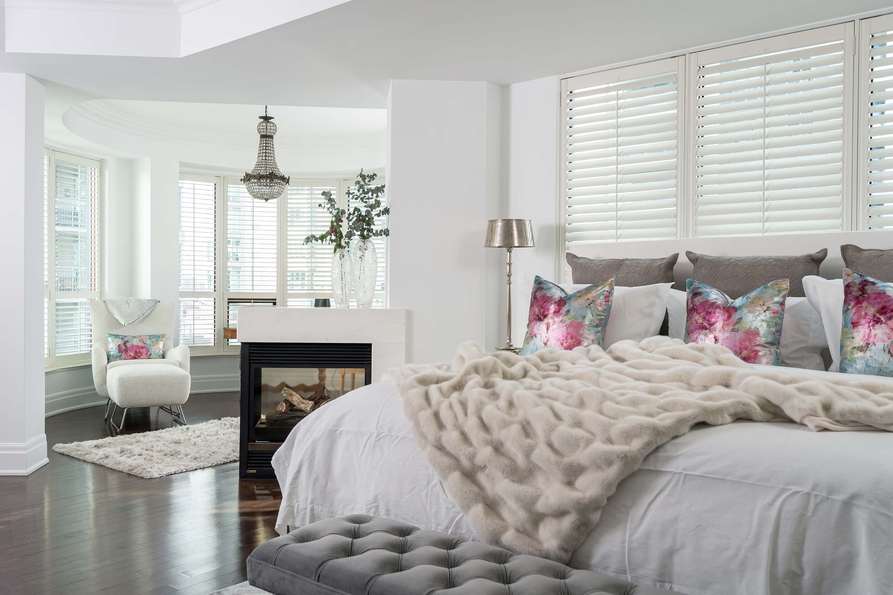 Interior of a bedroom with a bed, chair and fireplace. Several windows as well.